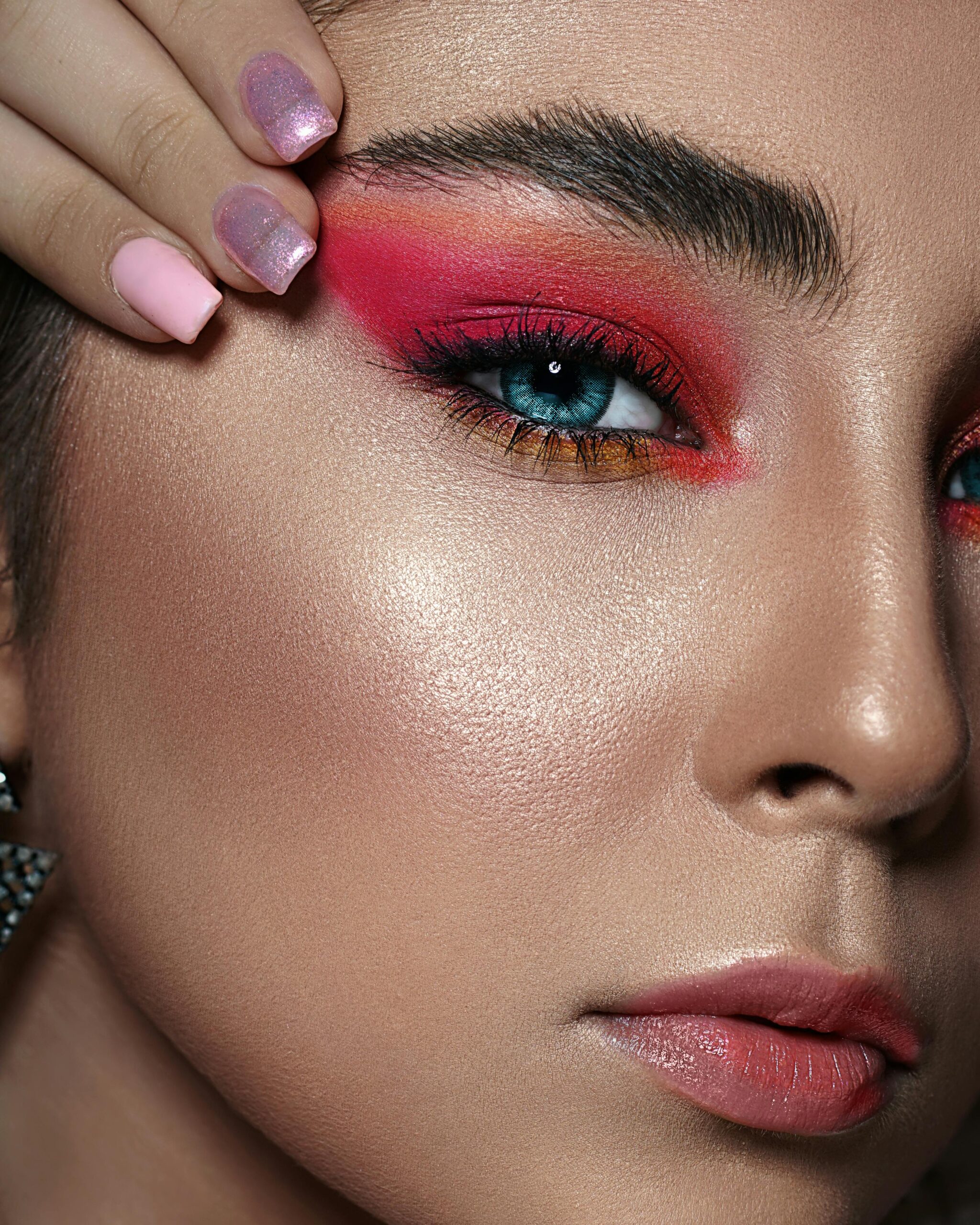 Close-up of a woman with bold makeup; featuring pink eyeshadow and blue eyes.